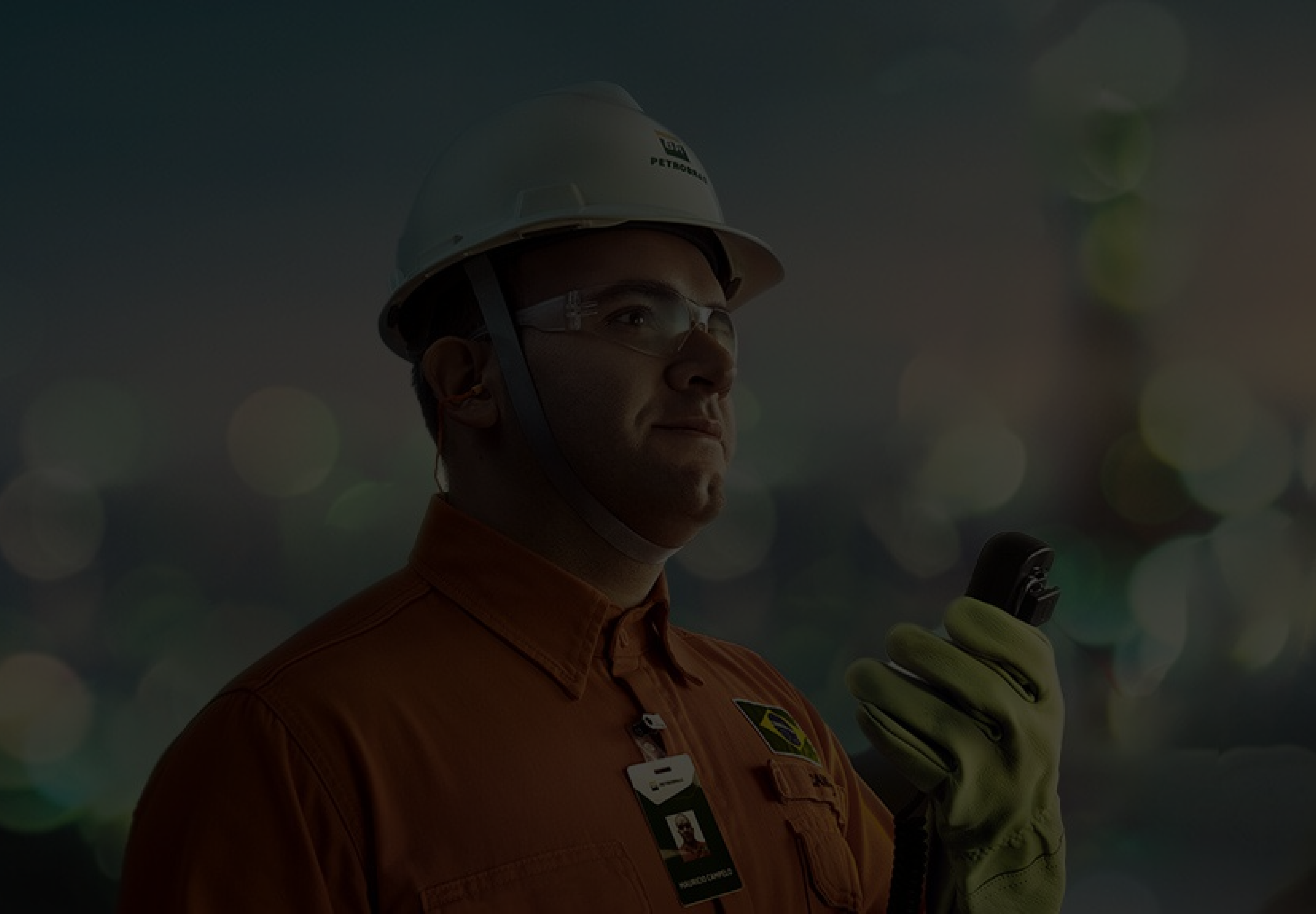 Um homem usando uniforme da Petrobras e segurando um walkie talkie com sua mão esquerda.