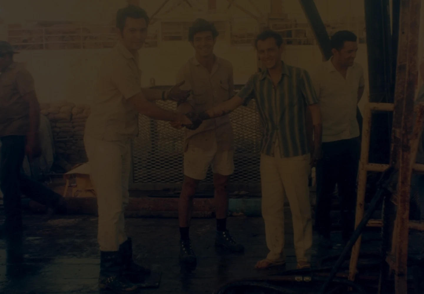 Foto antiga de três homens se cumprimentando enquanto olham para a câmera em plataforma no campo de Guaricema.