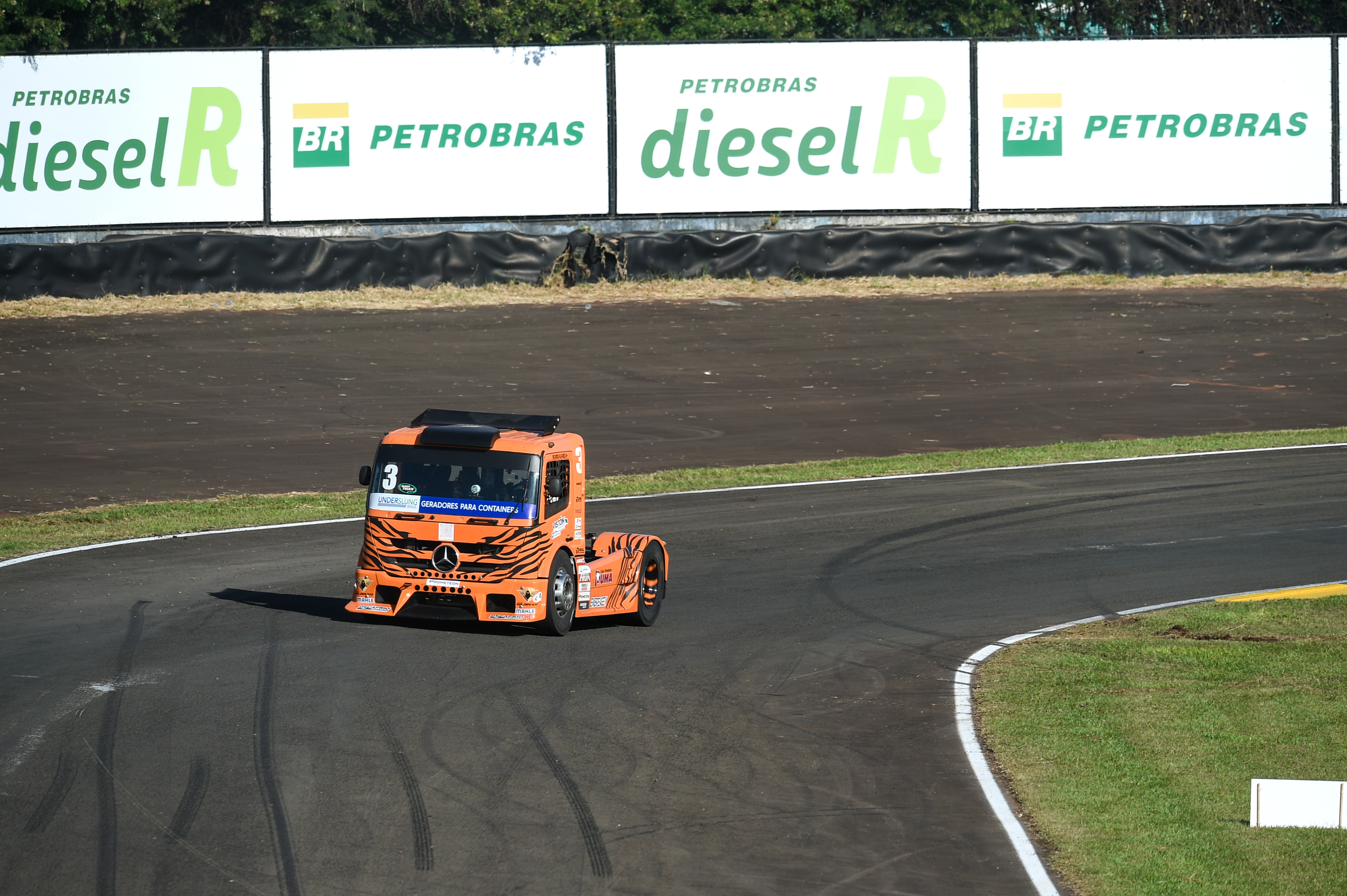 caminhão laranja em pista de corrida com placa de diesel R e Petrobras