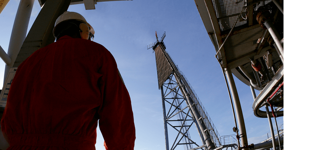 Fotografia diurna de um operador da Petrobras em uma plataforma de petróleo. Ele está de costas e usa uniforme.