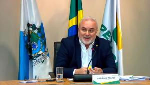 Presidente Jean Paul Prates, sentado no meio de duas bandeiras, com um microfone de mesa na sua frente.